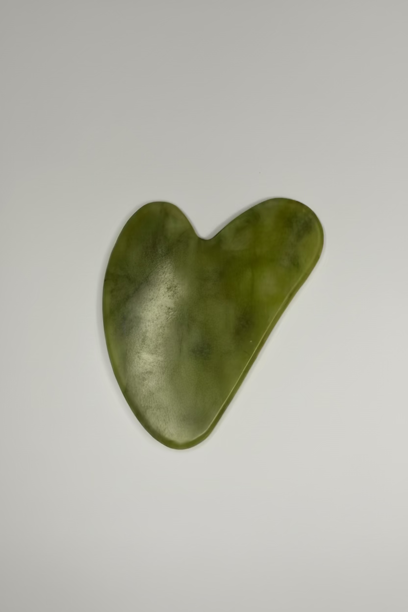 A heart-shaped jade Gua Sha massage tool made of polished green jade, shown on a neutral light gray background.
