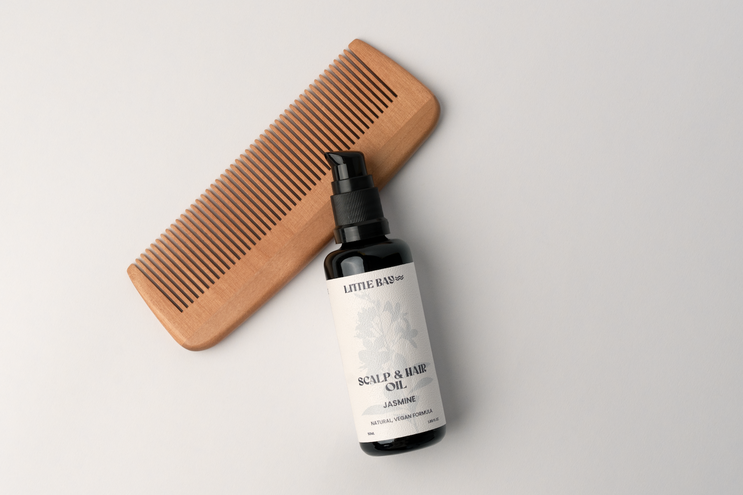 Wooden comb and bottle of scalp and hair care product on a light gray background